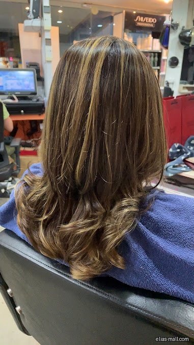 A woman's highlighted brown hair is styled in loose curls at a salon.