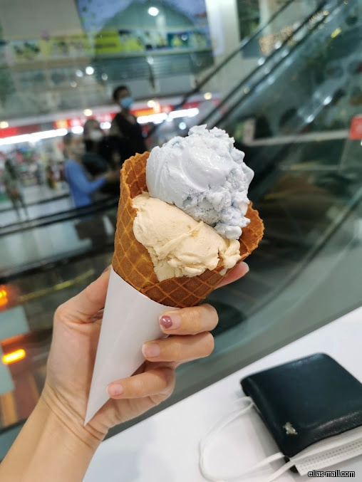 A hand holds a waffle cone with two scoops of ice cream.