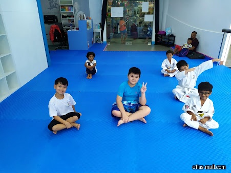 Children sit on a blue mat in a Taekwondo studio.