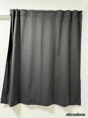 A gray curtain hangs from a white rod against a white wall.