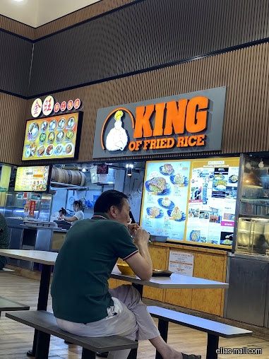 A man eats at King Of Fried Rice with menu boards above.