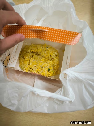 Fried rice in a takeout container inside a plastic bag.