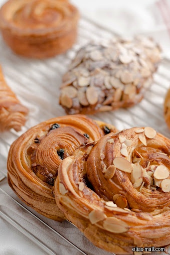 Close-up of pastries with almonds and raisins on a cooling rack.