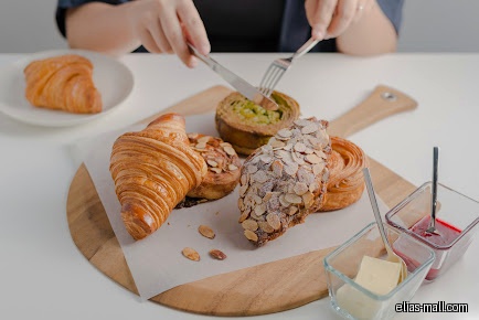 Pastries on a wooden board with butter and jam, being cut.