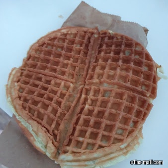 A close-up shot of a waffle from PrimaDéli in a paper wrapper.