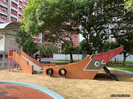 A boat-shaped playground structure with slides and tires in a sandy area.