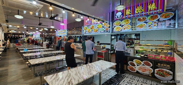 Interior of a restaurant with tables, customers, and a food display counter.