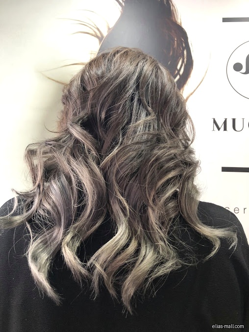 A woman with wavy, highlighted hair stands in front of a logo.