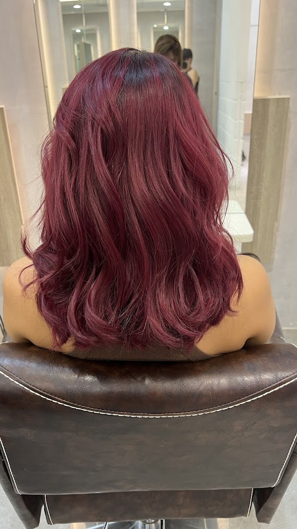 A person with vibrant red, wavy hair sitting in a salon chair, showcasing a fresh hair color.