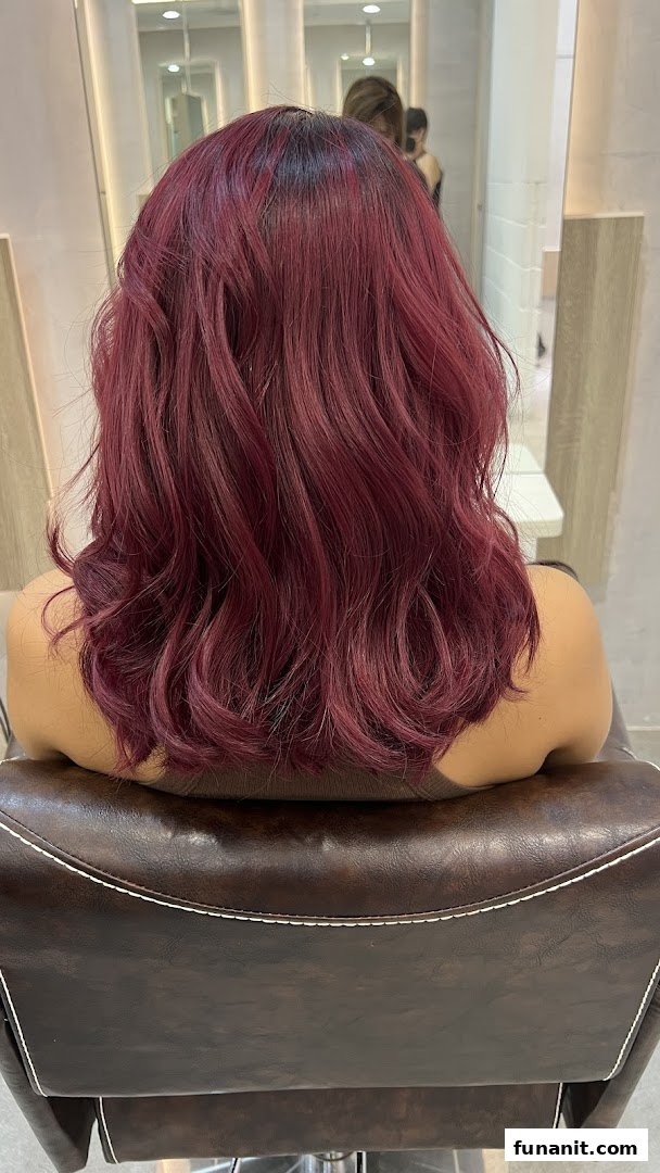 A person with vibrant red, wavy hair sitting in a salon chair, showcasing a fresh hair color.
