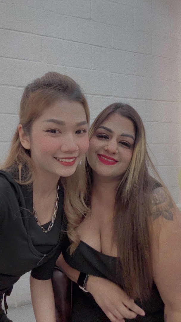Two smiling women, possibly staff or customers, pose for a photo against a white brick wall.