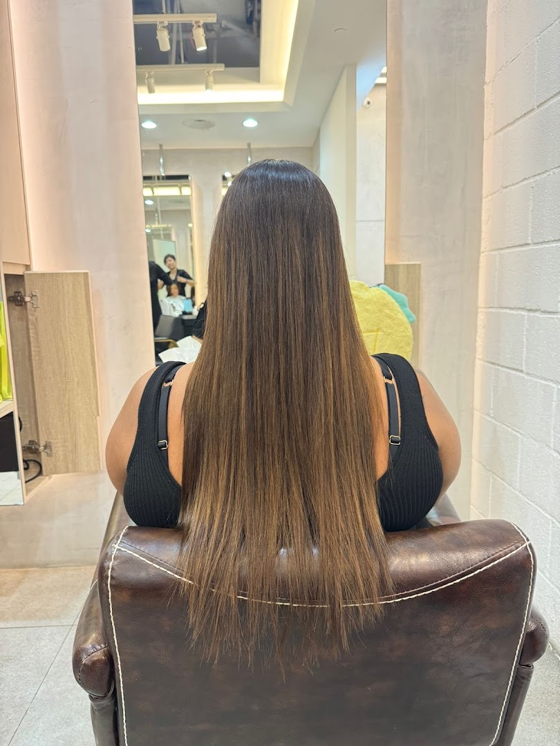 A customer with long, straight hair seated in a salon chair, reflecting a stylist at work.