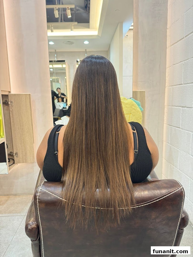 A customer with long, straight hair seated in a salon chair, reflecting a stylist at work.