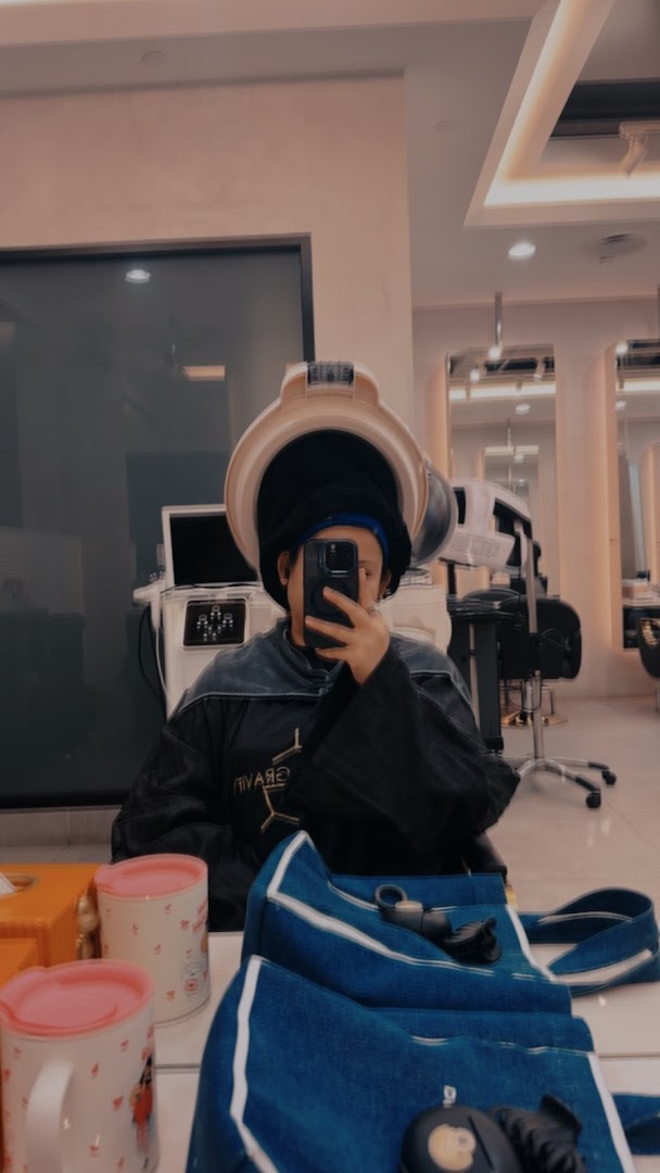 A person under a hair dryer takes a selfie in a modern salon, showcasing a relaxing beauty experience.