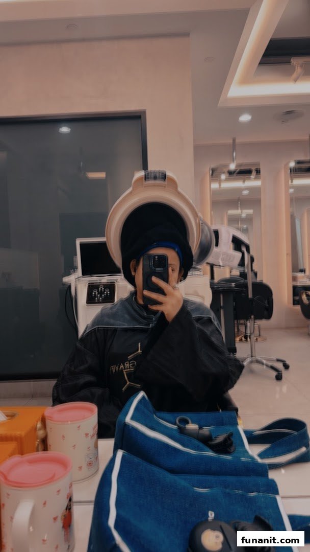 A person under a hair dryer takes a selfie in a modern salon, showcasing a relaxing beauty experience.