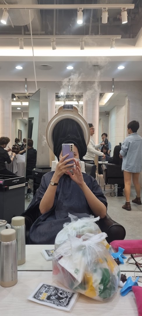 A customer takes a selfie while receiving a hair treatment with a steamer at a salon.