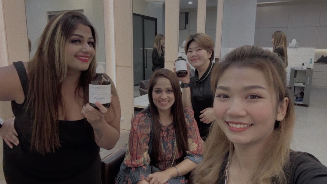 Four smiling women in a salon, two holding hair care products, showcasing a friendly atmosphere.