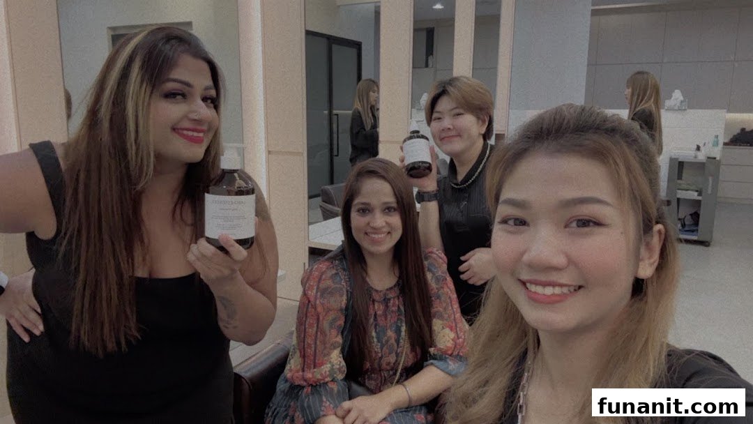 Four smiling women in a salon, two holding hair care products, showcasing a friendly atmosphere.