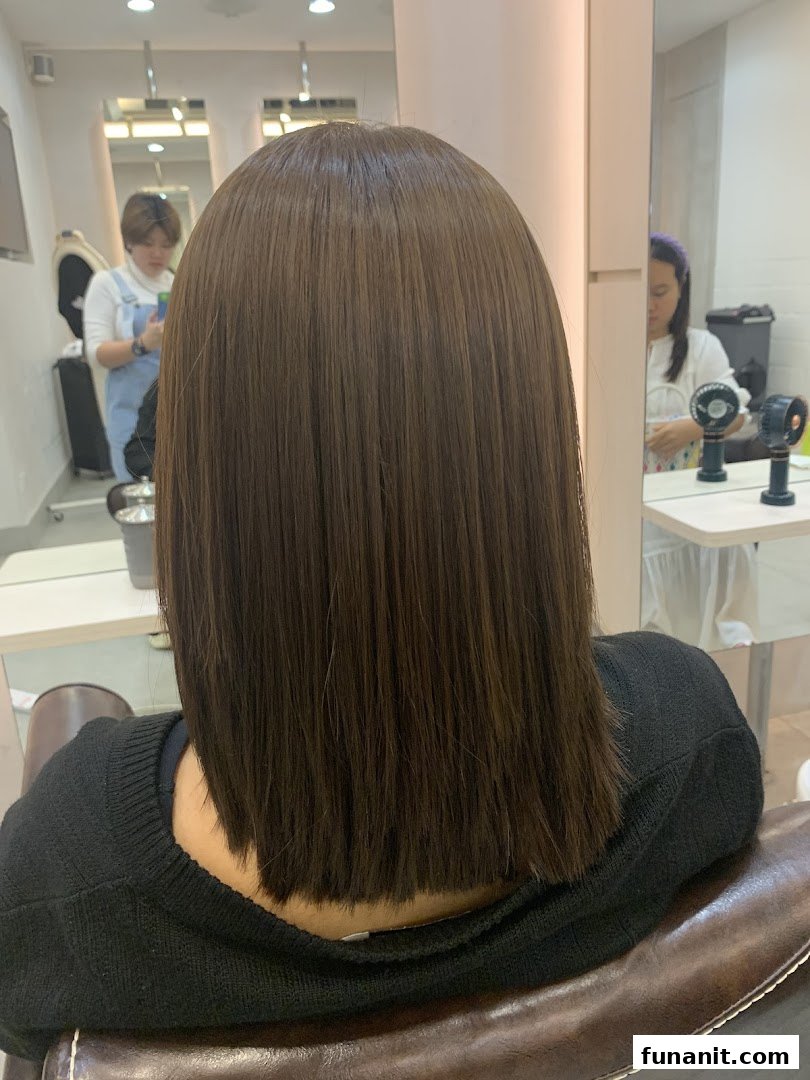 A customer's freshly styled, straight brown hair from the back, inside a modern hair salon.
