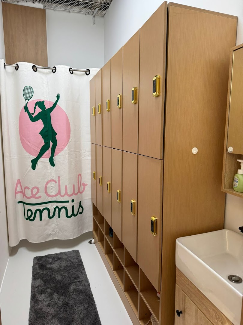 Interior view of Ace Club Tennis changing room with lockers, a themed curtain, and a sink.