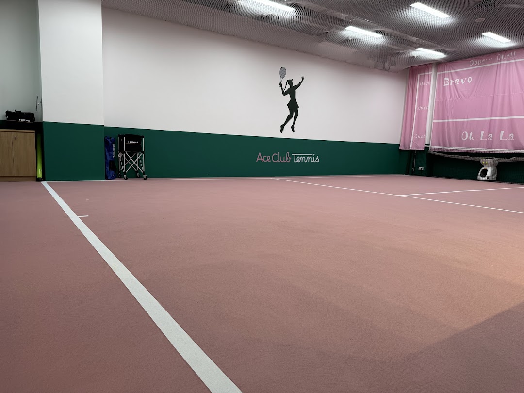 An indoor tennis court at Ace Club Tennis, featuring pink flooring, green walls, and a player silhouette logo.