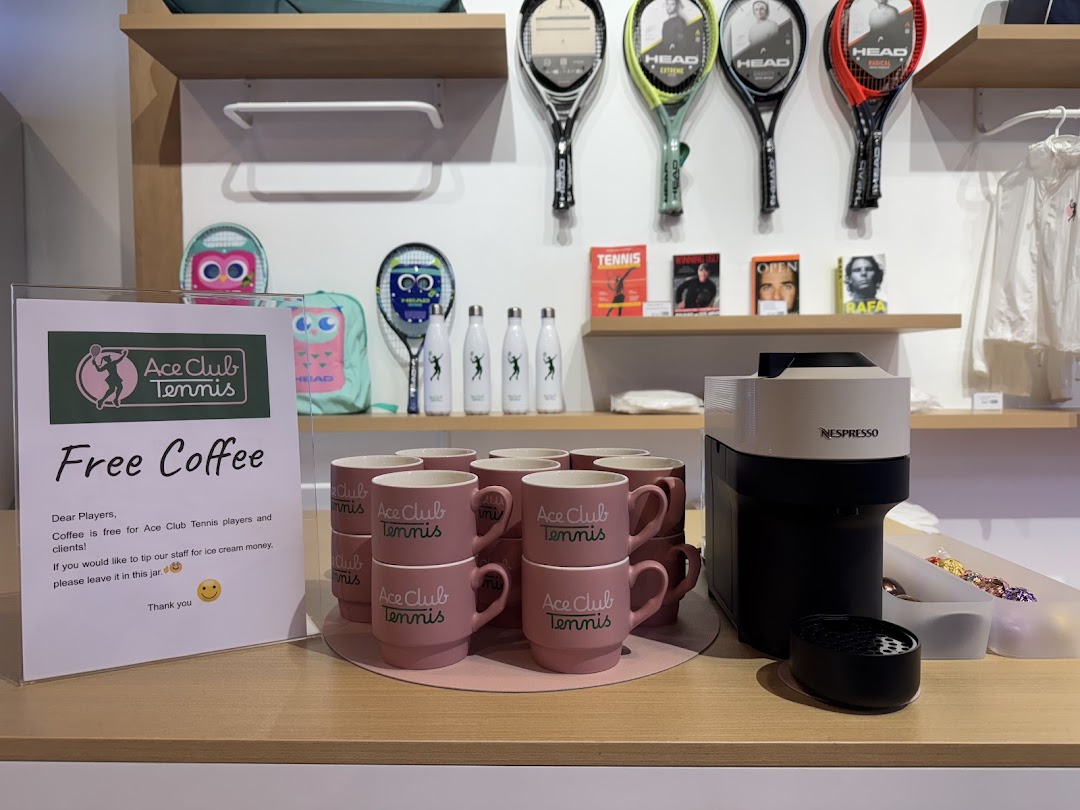 A complimentary coffee station with branded mugs and a 'Free Coffee' sign inside Ace Club Tennis.