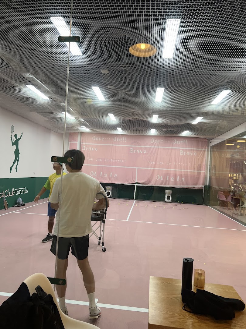 Two individuals on a vibrant pink indoor tennis court, possibly training or playing.
