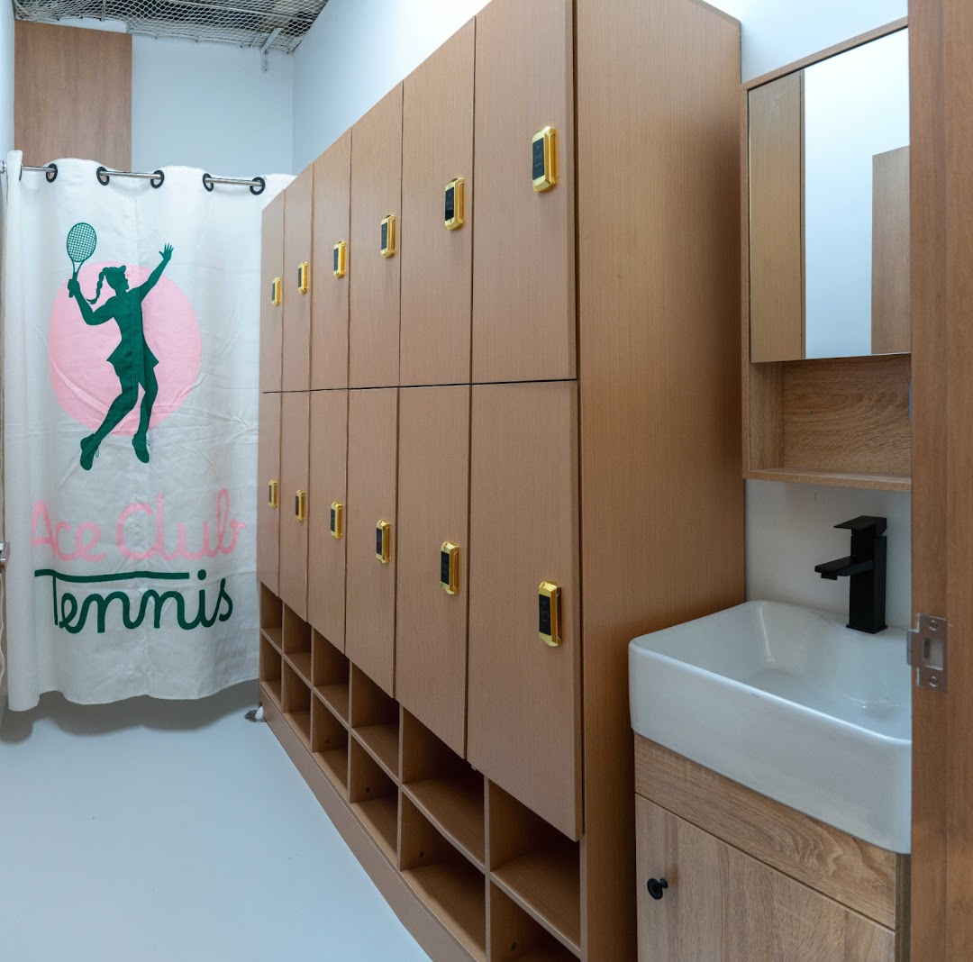A modern changing room with wooden lockers, a sink, and a branded shower curtain.