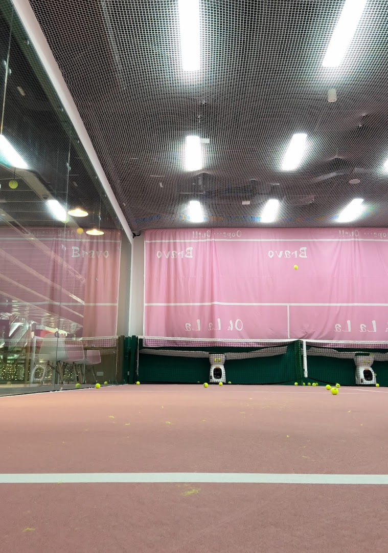 An indoor pink tennis or padel court with scattered tennis balls and ball machines under bright lights.