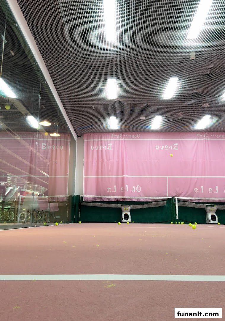 An indoor pink tennis or padel court with scattered tennis balls and ball machines under bright lights.