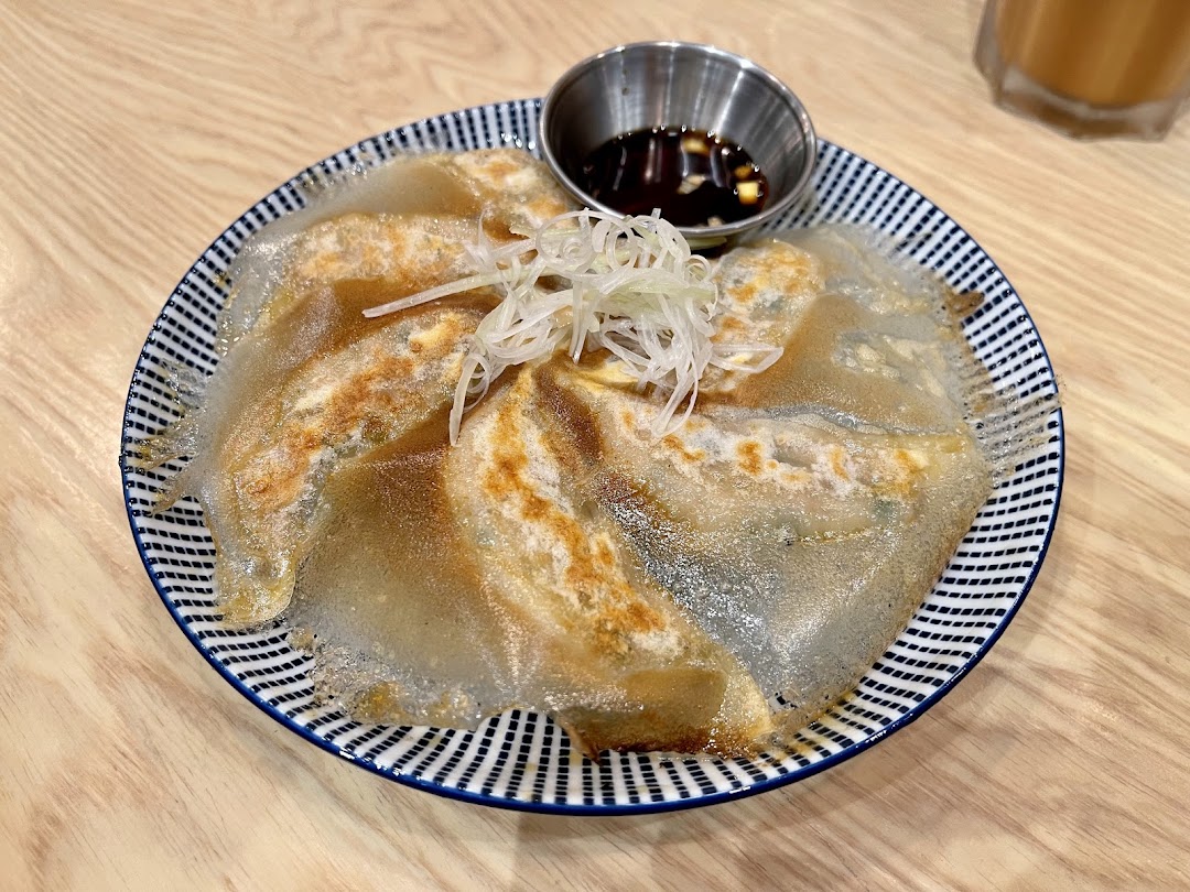 A plate of crispy-skirt gyoza with a dipping sauce and shredded scallions on a patterned plate.