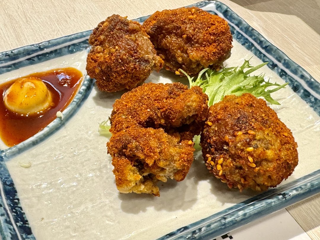 Close-up of crispy, golden-brown fried items with a rich dipping sauce and fresh lettuce on a decorative plate.