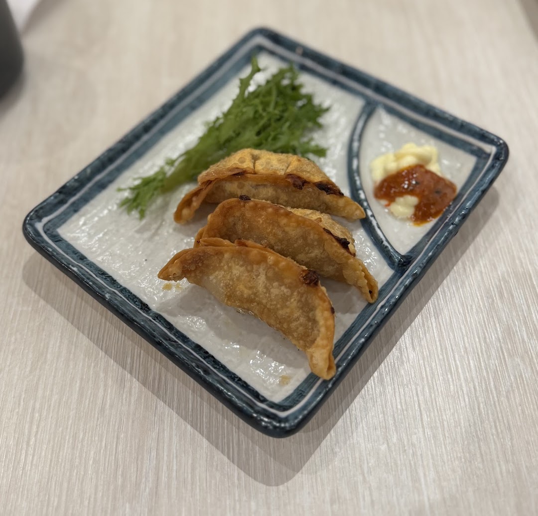 A plate of crispy fried dumplings with fresh greens and two dipping sauces.
