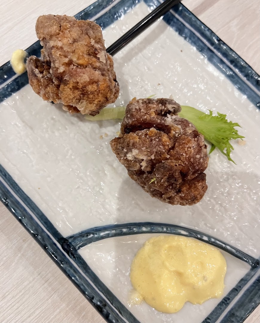 A close-up of two pieces of crispy fried chicken (karaage) served with a creamy dipping sauce on a decorative plate.