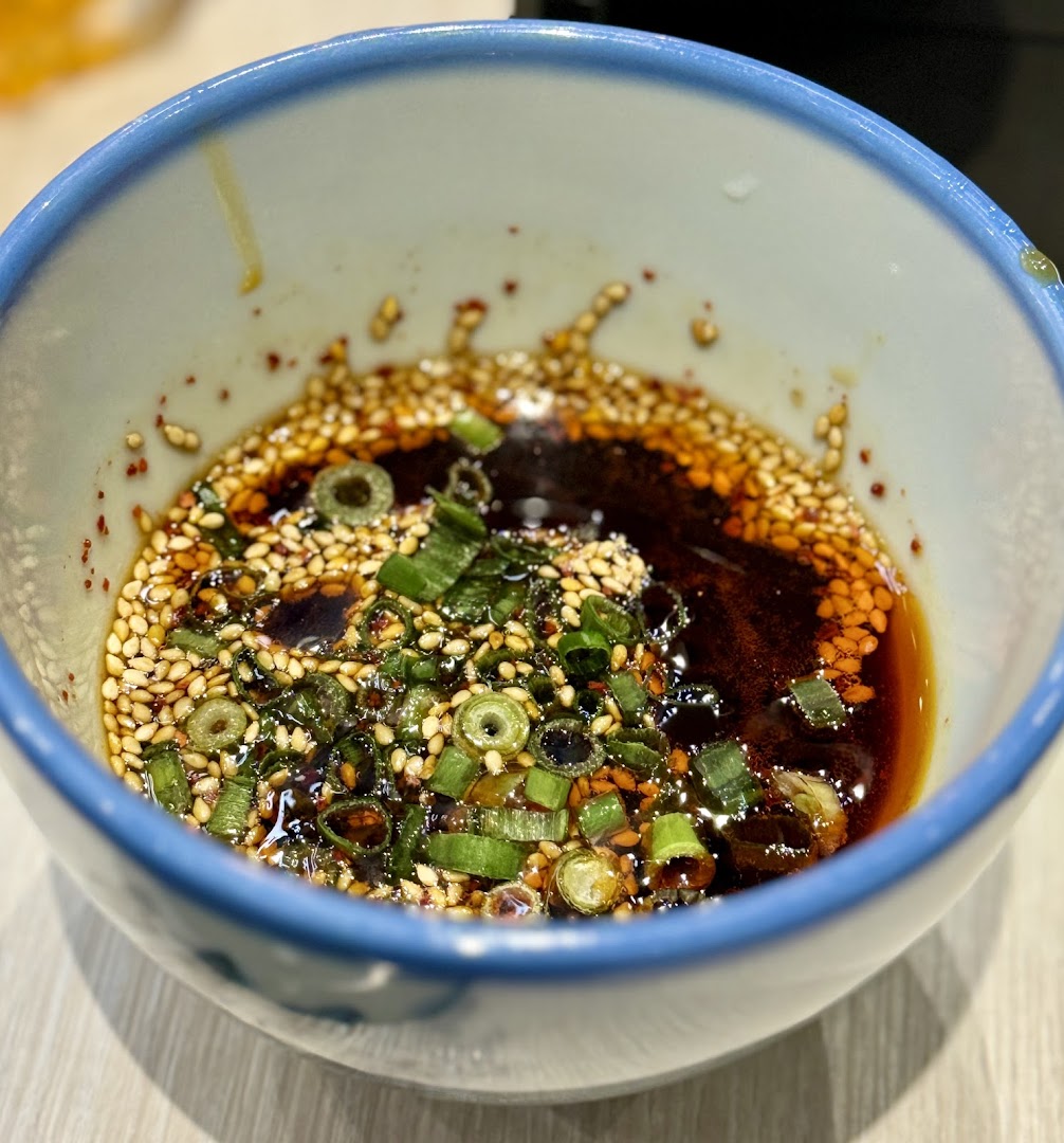 A close-up of a flavorful dipping sauce with sesame seeds and green onions in a bowl.