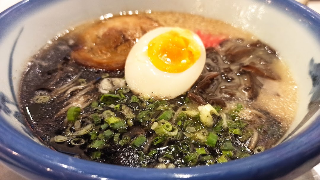 A close-up of a delicious bowl of ramen with a soft-boiled egg, pork, and green onions.