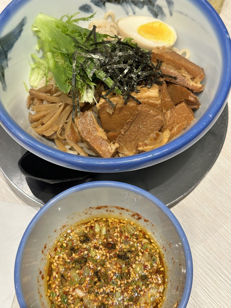 A close-up of a delicious bowl of ramen with pork, egg, seaweed, and a side of dipping sauce.