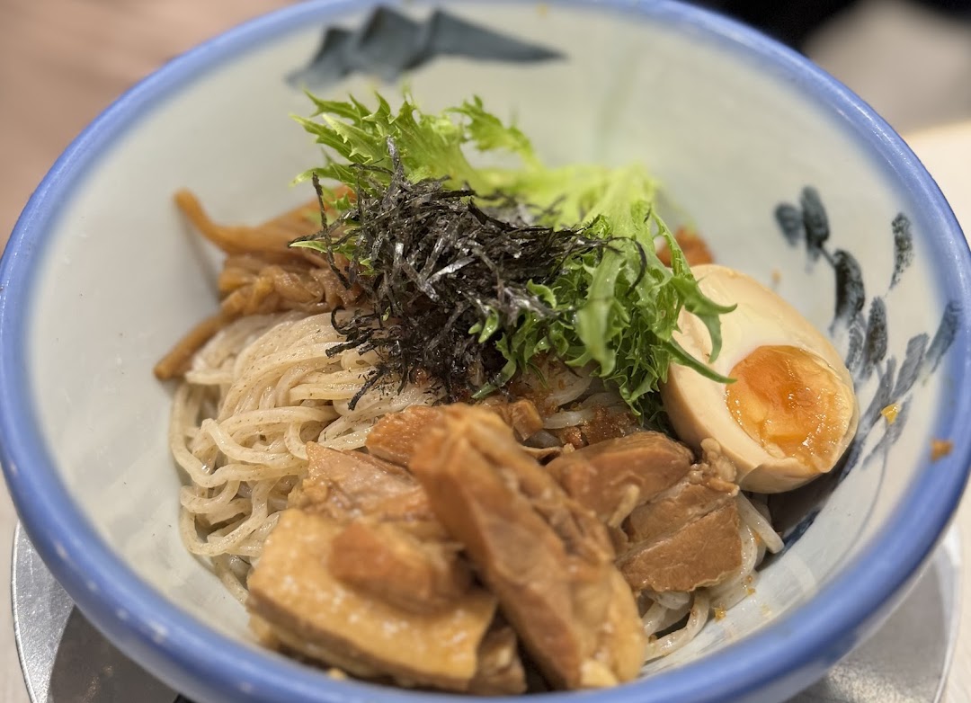 A close-up of a delicious bowl of ramen or tsukemen with pork, egg, and greens.
