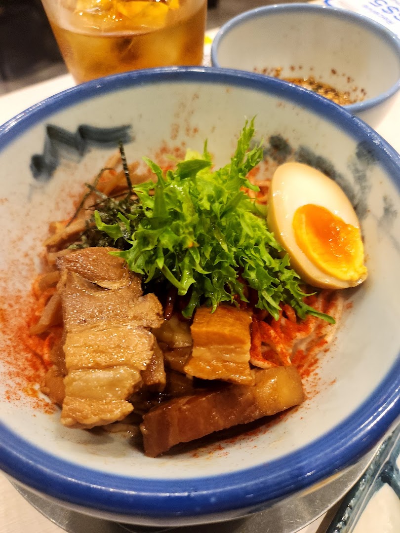 A close-up of a delicious ramen or noodle dish featuring tender pork belly, a soft-boiled egg, and fresh greens.