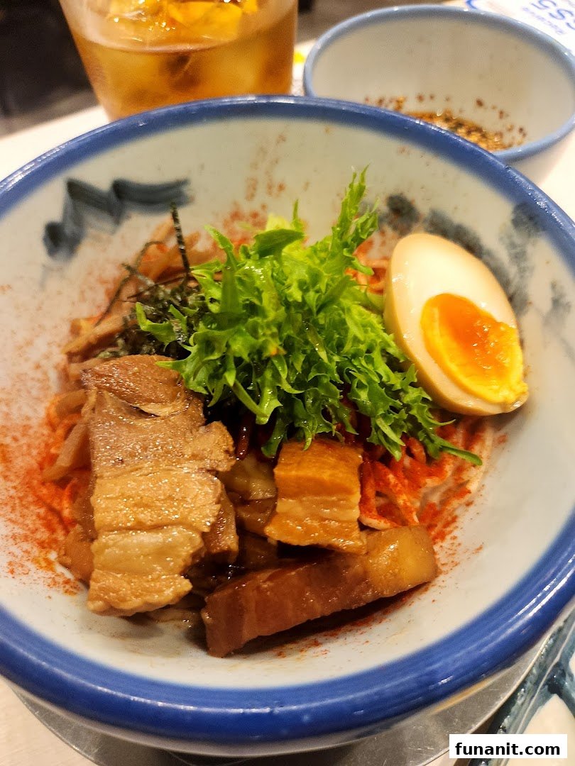 A close-up of a delicious ramen or noodle dish featuring tender pork belly, a soft-boiled egg, and fresh greens.