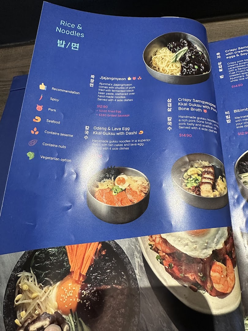 A detailed menu page from Ajummas, showcasing various Korean noodle and rice dishes with descriptions and prices.