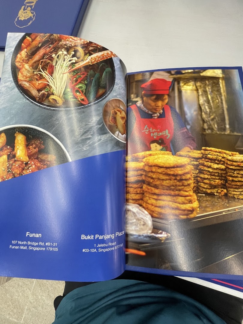 An open brochure showcasing vibrant Korean dishes like seafood stew and tteokbokki, with shop location details.