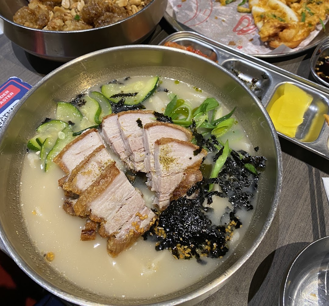A close-up of a delicious Korean noodle soup with crispy pork belly, zucchini, and seaweed.