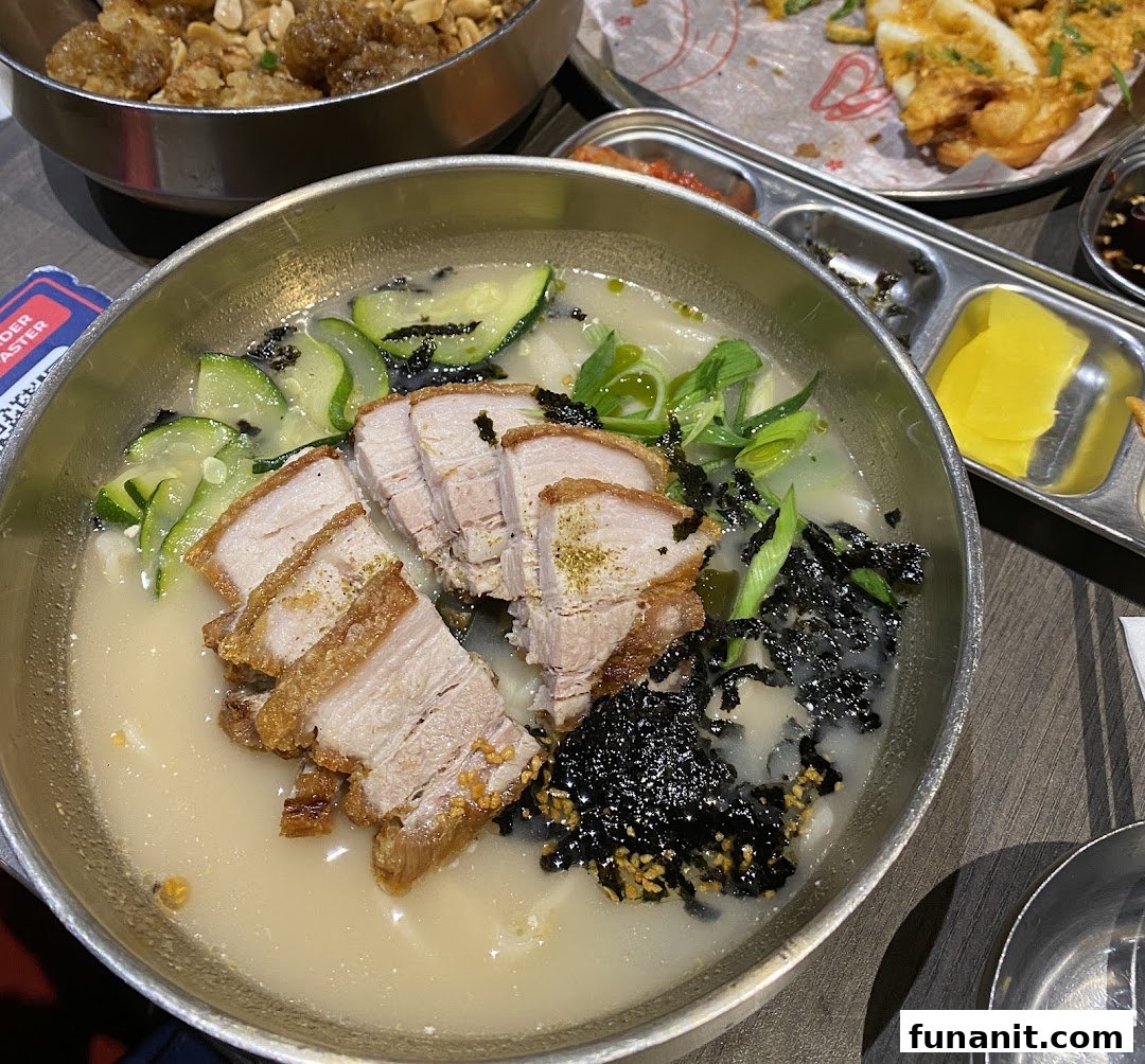 A close-up of a delicious Korean noodle soup with crispy pork belly, zucchini, and seaweed.