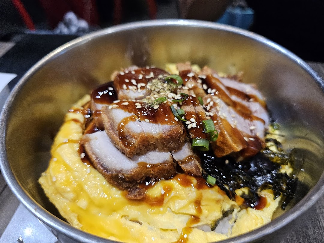 A close-up of a delicious rice bowl with crispy pork, scrambled egg, and seaweed.