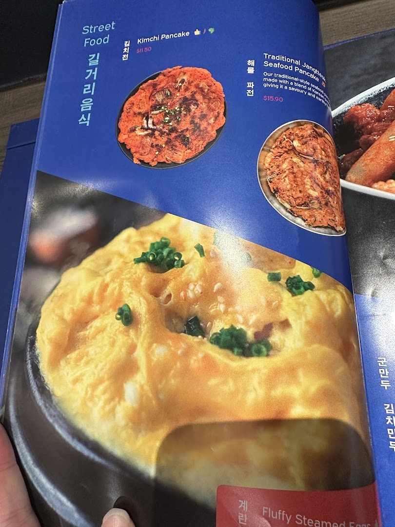 A close-up of a Korean restaurant menu featuring savory pancakes and fluffy steamed eggs.