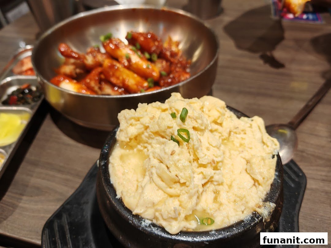 Close-up of delicious Korean steamed egg and spicy rice cakes with banchan on a wooden table.