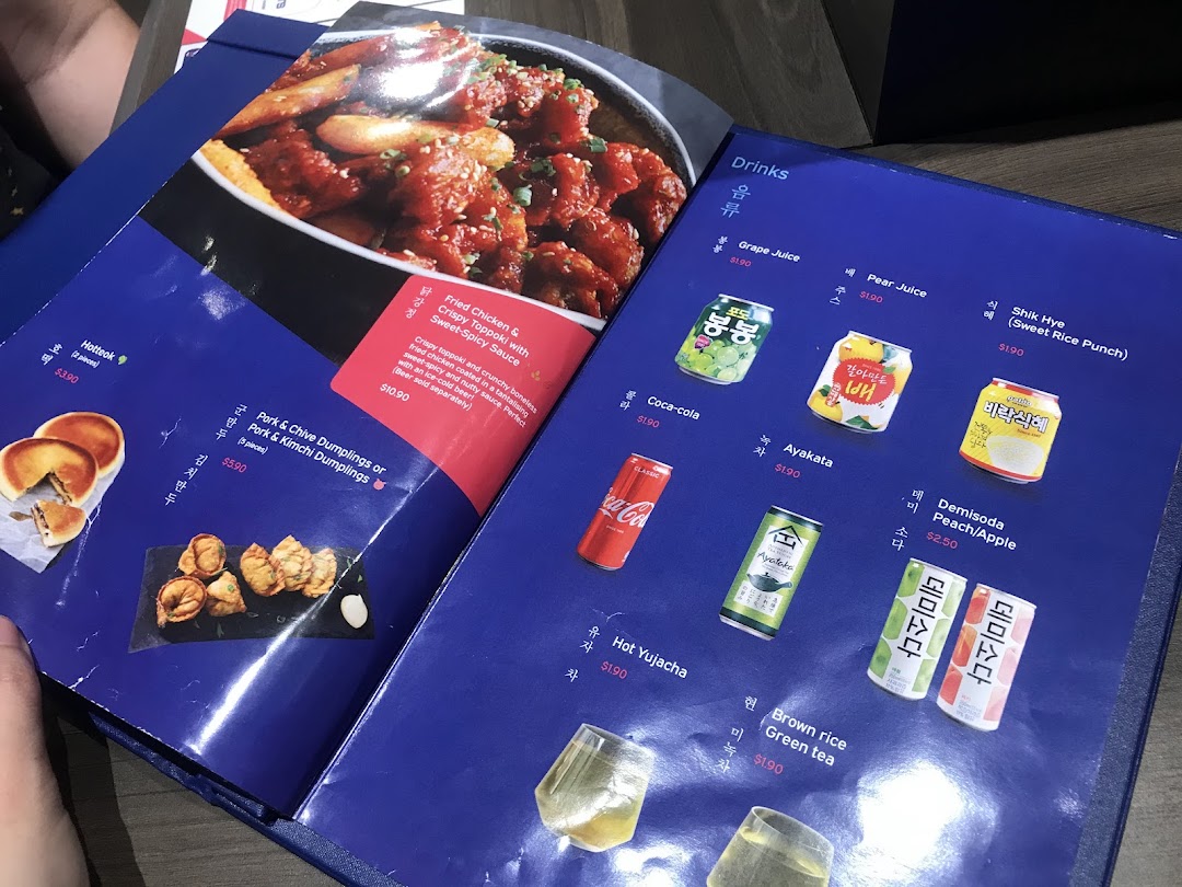 A close-up view of a vibrant blue menu from Ajummas, showcasing Korean food and drink options.