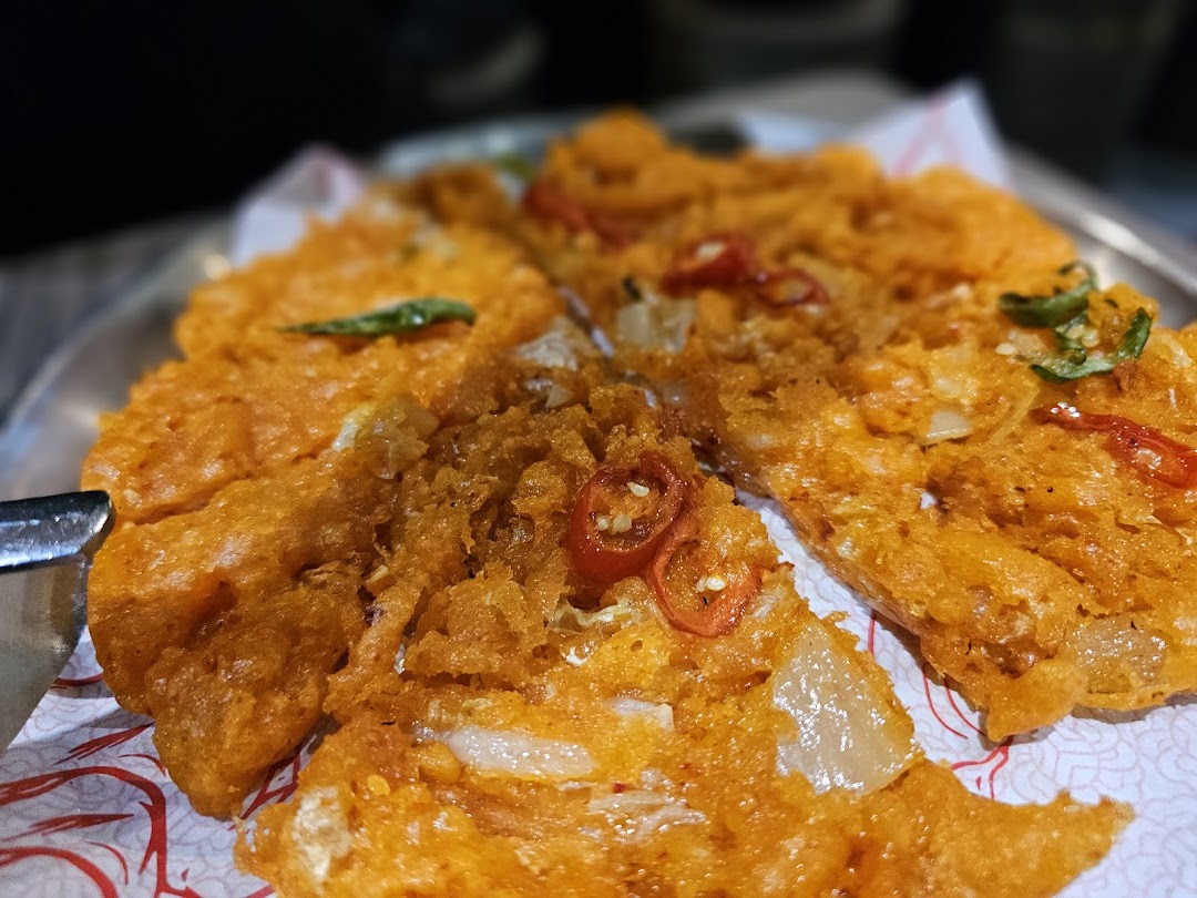 A close-up of a vibrant orange, crispy Korean pancake garnished with chili and herbs.