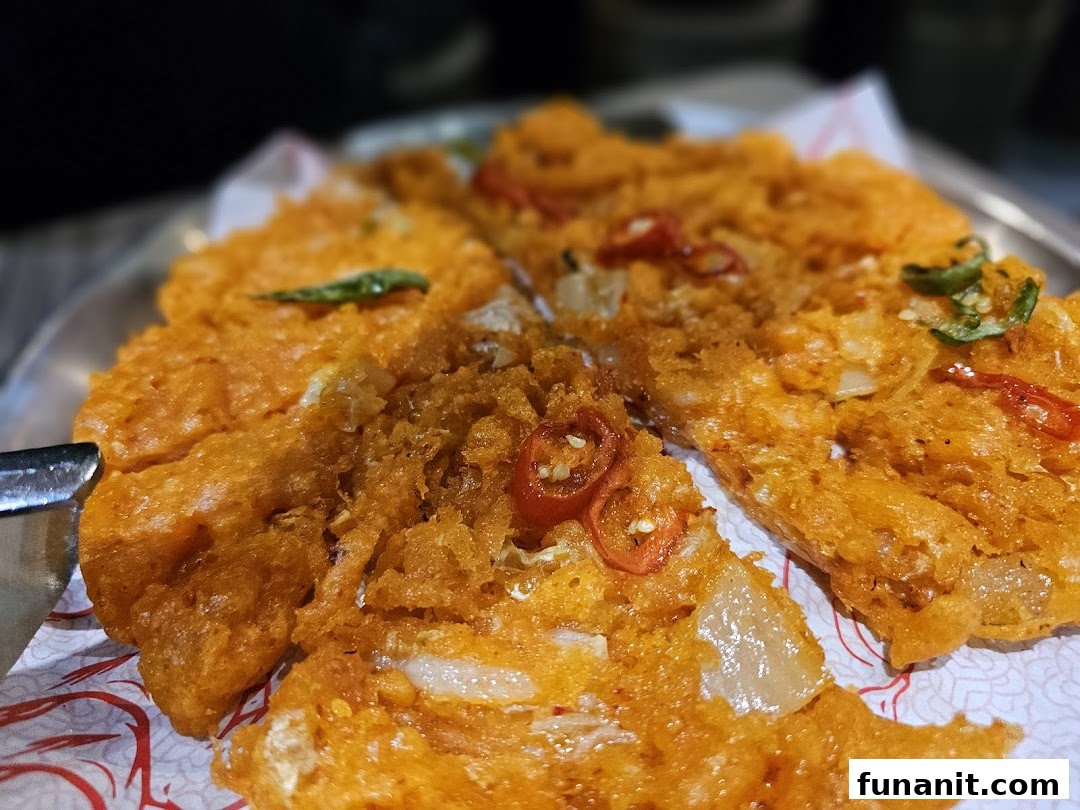 A close-up of a vibrant orange, crispy Korean pancake garnished with chili and herbs.